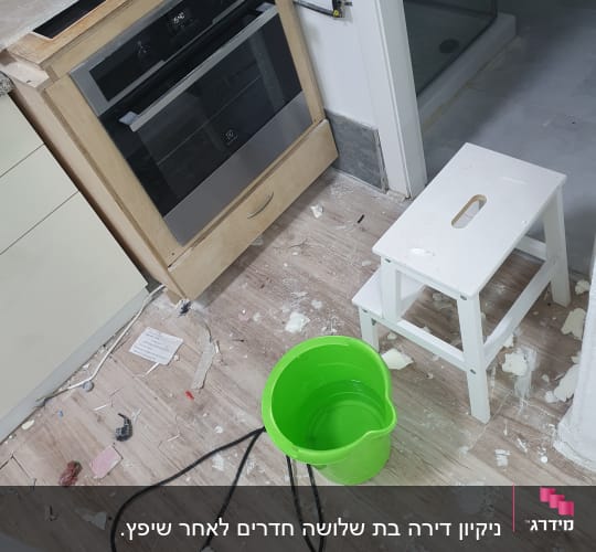 דלי ירוק על רצפה מלוכלכת עם לכלוך וכלים